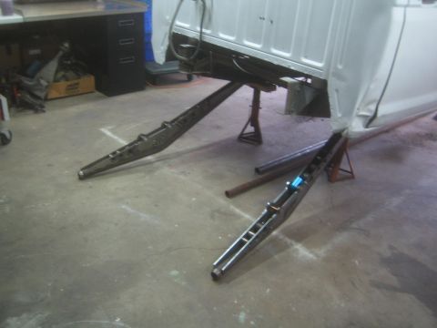 1990 Ford Bronco - Photograph of fabricated steel frame rails on a shop floor next to a truck cab, not a document.