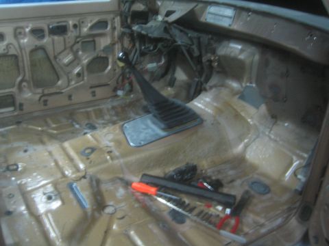 1990 Ford Bronco - Photograph of a stripped vehicle interior floor pan with shifter and exposed wiring, not a document.