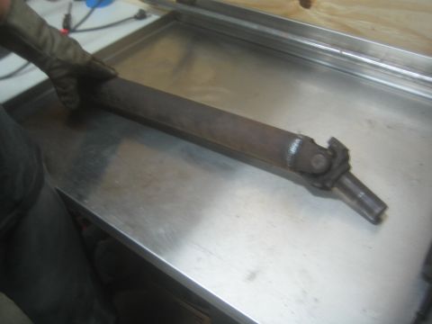 1987 Suzuki Samurai - Photo of a vehicle driveshaft with a universal joint resting on a steel workbench, held by a gloved hand.