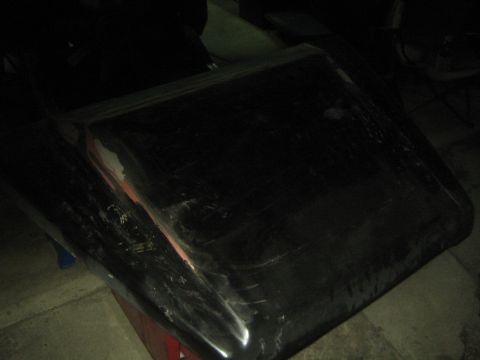 1987 Suzuki Samurai - Photo of a dark vehicle hood panel resting on a bench in a dimly lit shop.