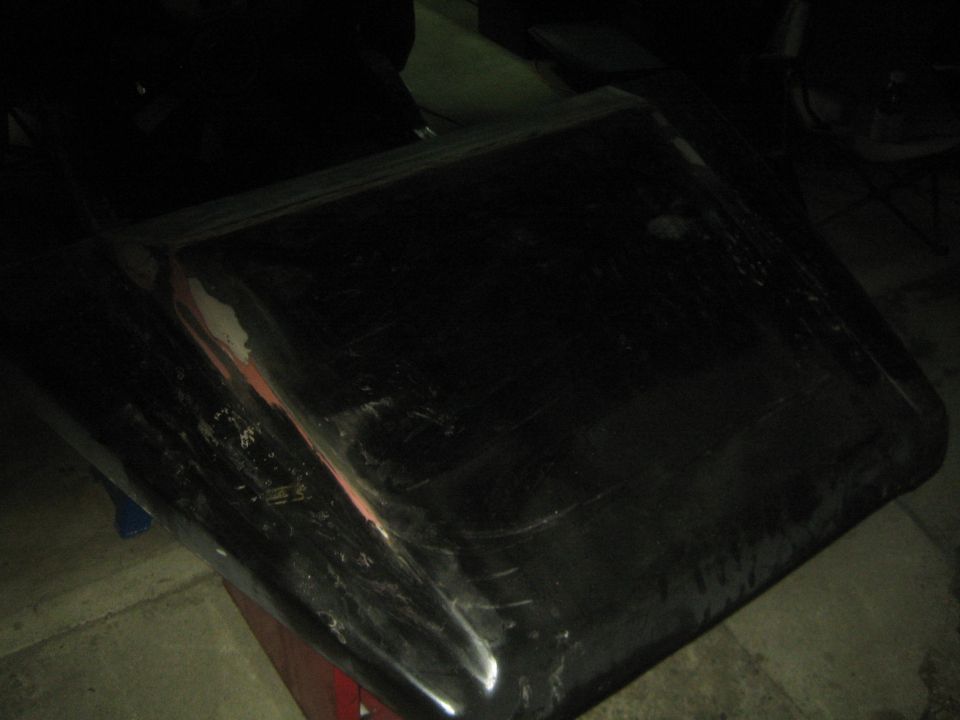 Black vehicle hood lying on a workbench in dim light