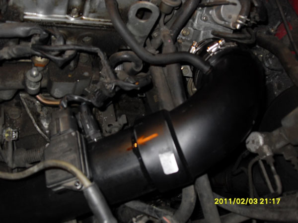 Black aftermarket intake tube routed through a dirty engine bay