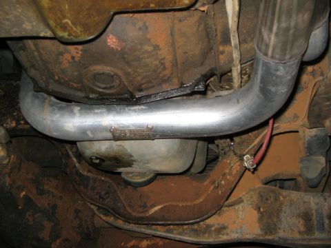 1991 Ford Bronco - Close-up of an exhaust pipe with a visible manufacturer's tag, showing rust on the vehicle's undercarriage.