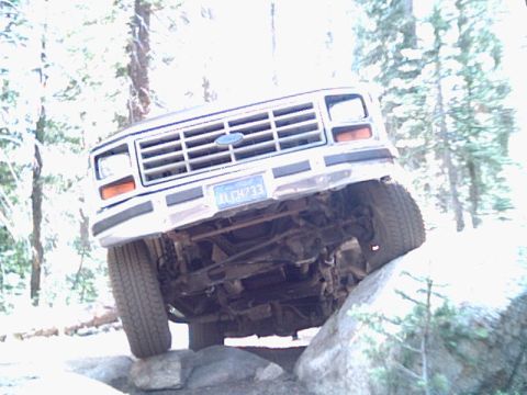 1985 Ford Bronco - A white Ford Bronco navigates rocky terrain, its undercarriage clearly visible.