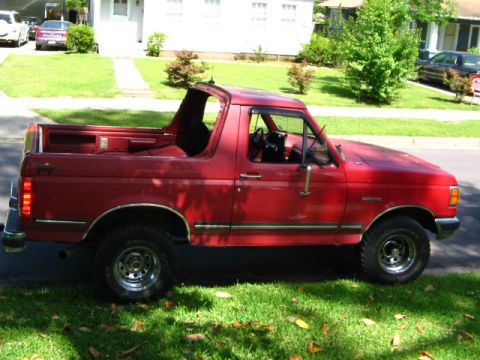 1991 Ford Bronco - A red Ford Bronco is parked on the side of the road with its top removed.
