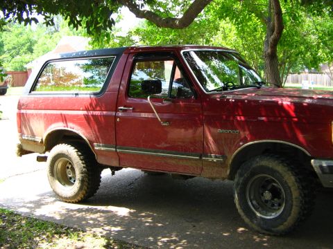 1991 Ford Bronco - This red Ford Bronco, likely a 1992 model, is parked outdoors under a tree.