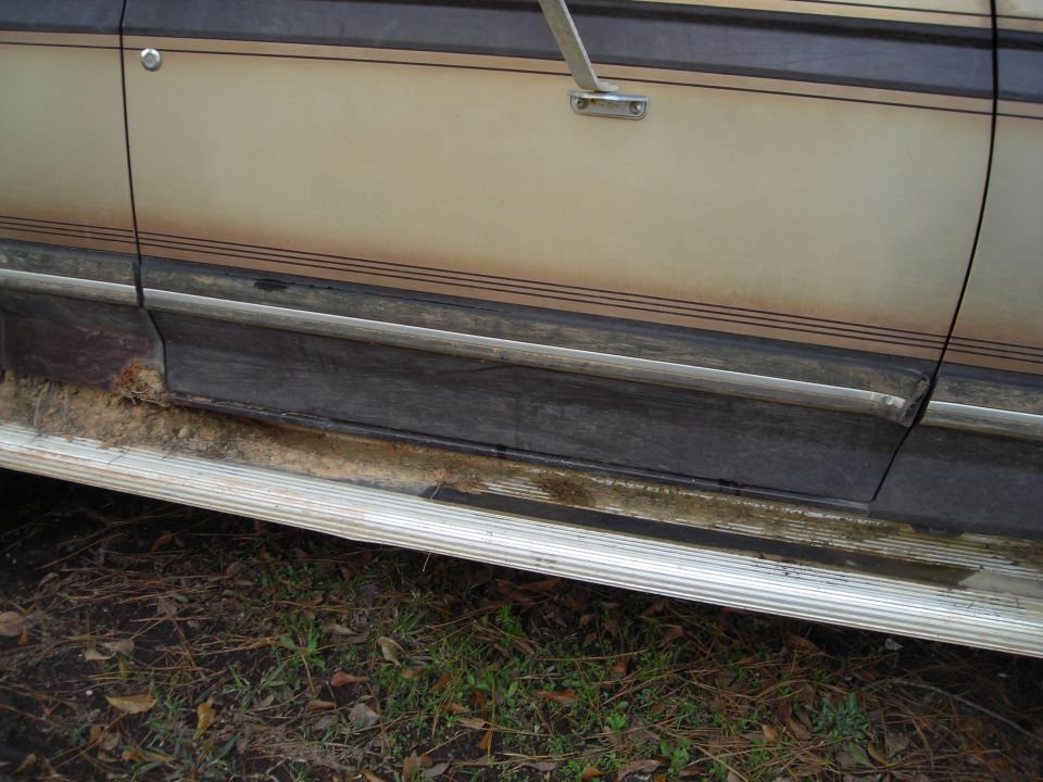Close-up of a vehicle's lower body panel and running board with rust and dirt.