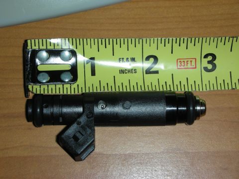 1998 Ford Crown Victoria - Photograph of a black fuel injector laid beside a tape measure to show its length.