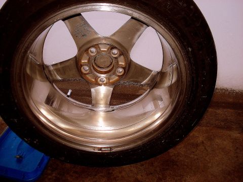 1998 Ford Taurus - A close-up, interior view of a shiny, silver alloy wheel with five spokes, mounted on a tire. The wheel is resting on a brown surface next…