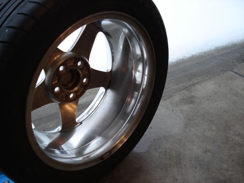 1998 Ford Taurus - A close-up view of a shiny, multi-spoke aftermarket wheel and tire, possibly from a 1998 Ford Taurus, resting on a concrete surface.