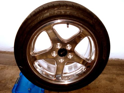 1998 Ford Taurus - A close-up view of a polished five-spoke alloy wheel with a tire mounted on it. The wheel has a black center cap with silver text that appe…