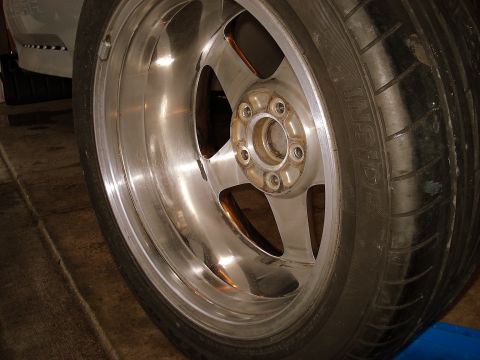 1998 Ford Taurus - A close-up, low-angle shot of the driver's side front wheel and tire of a vehicle. The shiny chrome rim has a multi-spoke design, and the t…