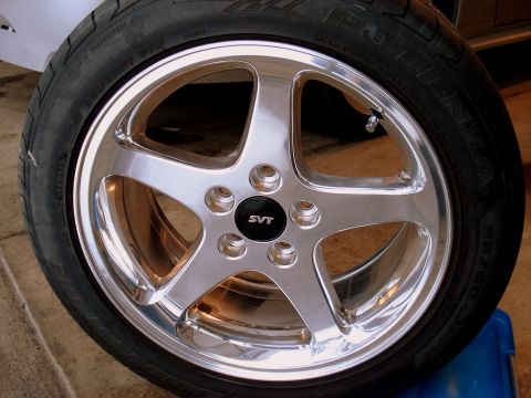 1998 Ford Taurus - A close-up, slightly angled view of a chrome 5-spoke wheel with a black SVT center cap, mounted on a tire with visible sidewall text. The w…