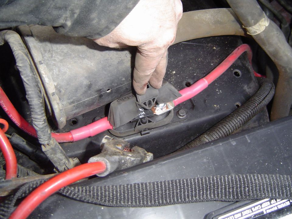 Hand opening a black fuse holder on a red battery cable in a Bronco engine bay