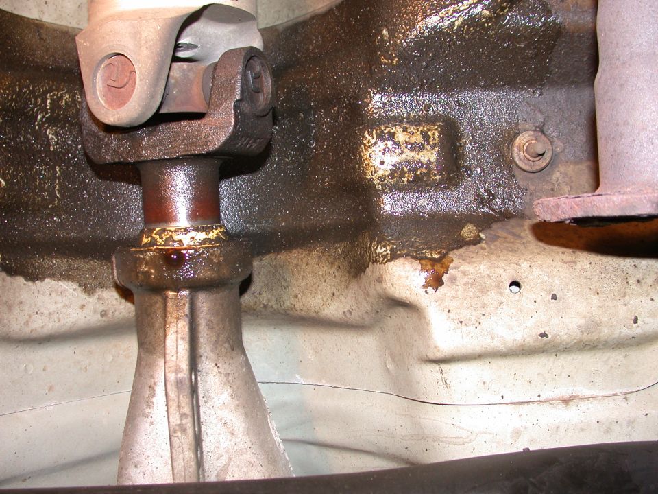 Underside of a vehicle showing a greasy driveshaft and universal joint.