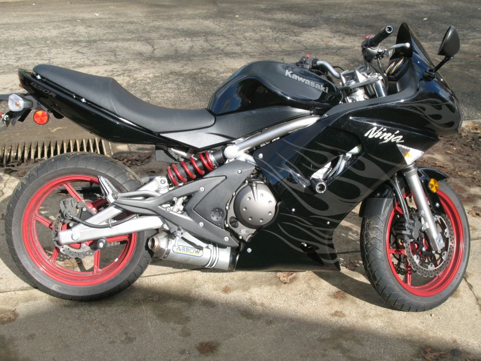 Black Kawasaki Ninja 650R motorcycle with red rims and flame graphics, parked outdoors.