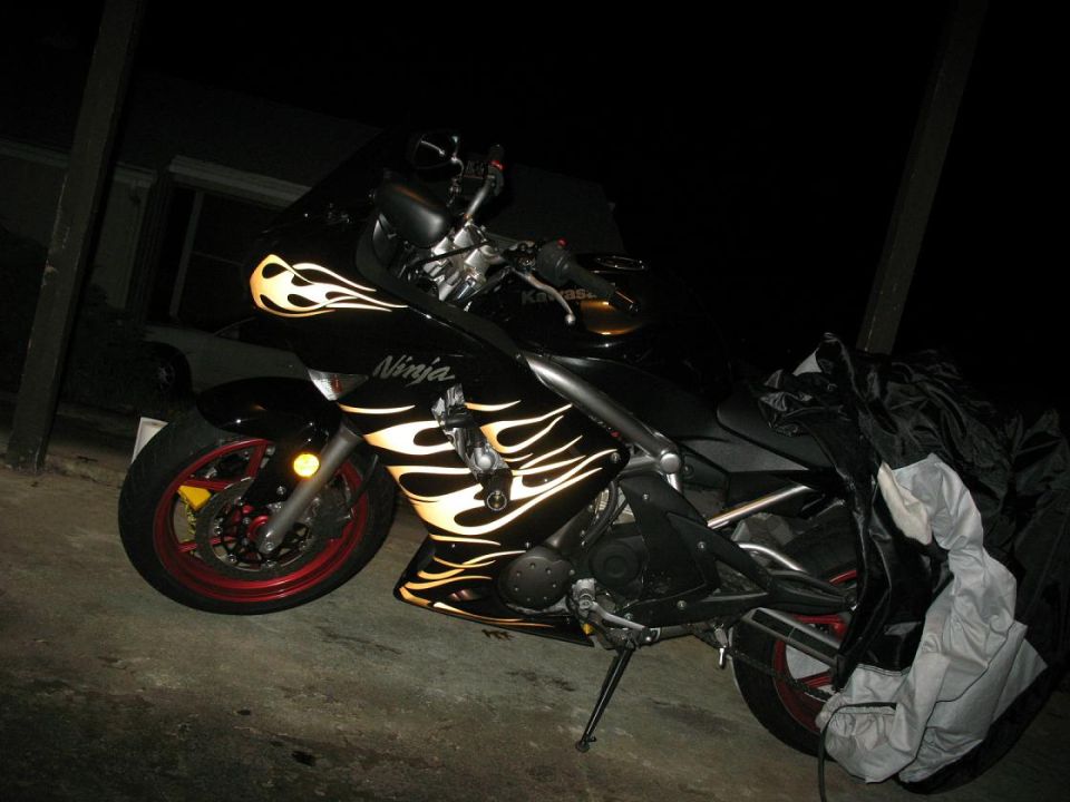 Black Kawasaki Ninja motorcycle with flame decals, parked at night, partially covered.