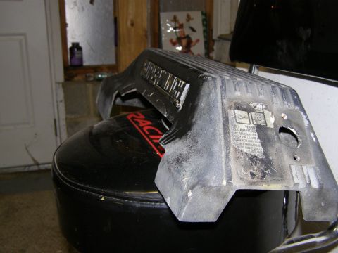 1993 Ford Bronco - A black plastic engine cover with raised lettering and a warning sticker is resting on a black round seat with a red 'RACING' decal. The co…