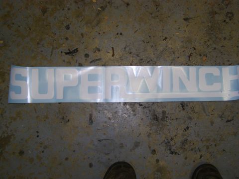 1993 Ford Bronco - A white Superwinch decal is laid out horizontally on a gray concrete floor. The decal features the word "SUPERWINCH" in large, bold, white…