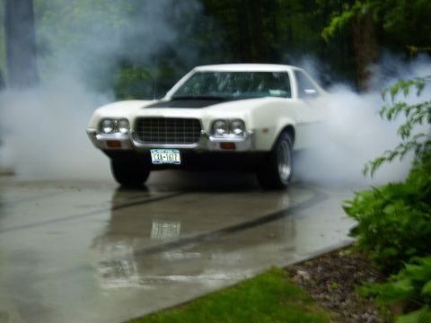1972 Ford Ranchero - A white early-1970s Ford Ranchero doing a smoky burnout on a wet concrete driveway, tire smoke billowing around the rear and dark rubber st…