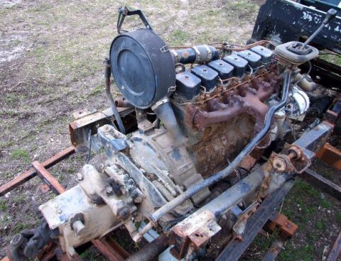 1989 Ford Bronco - Rusty Cummins 6BT engine and transmission assembly sits on wooden supports outdoors.