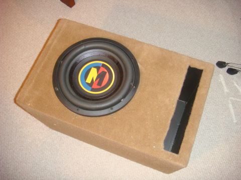 1996 Ford Bronco - A car subwoofer is housed in a tan carpeted enclosure, a prominent M logo.