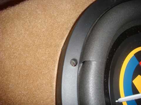 1996 Ford Bronco - A close-up view shows the edge of a subwoofer speaker with a torn surround, mounted within a tan carpeted enclosure.