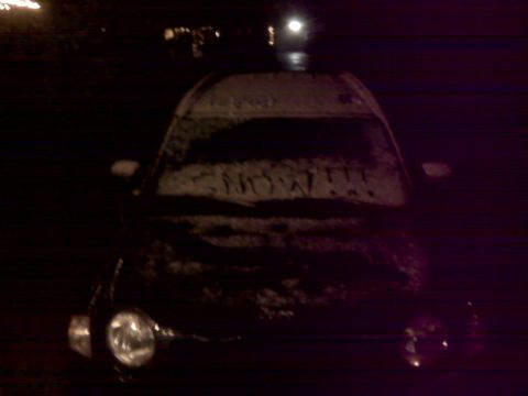 2008 Jeep Wrangler - A black Jeep Wrangler is seen from the front, covered in snow with its headlights illuminated.