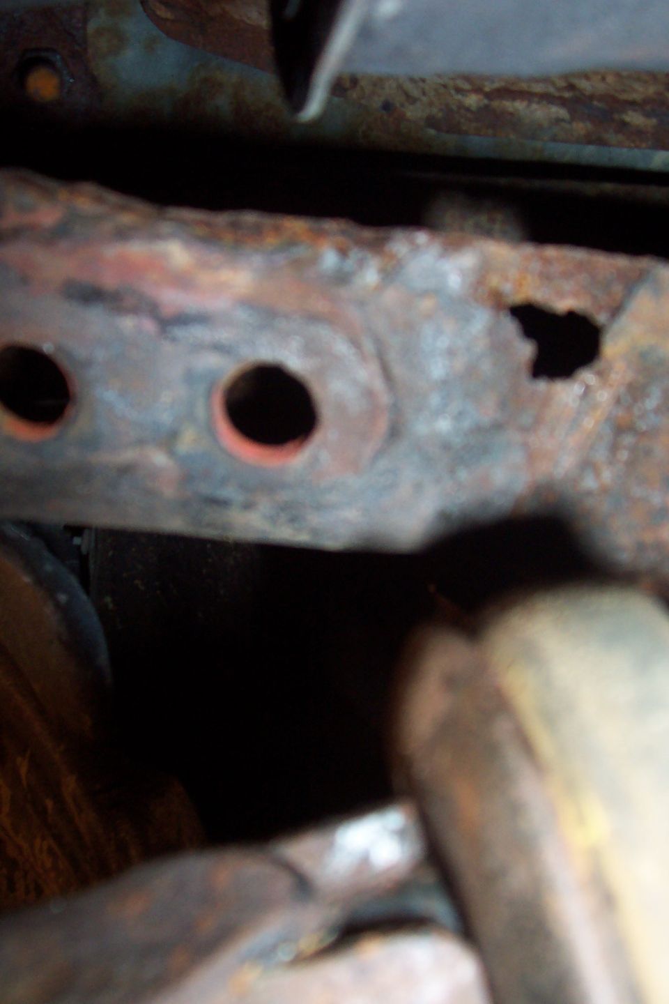 Close-up of rusted frame member with bolt holes and a rust-through hole on a 1990 Ford Bronco