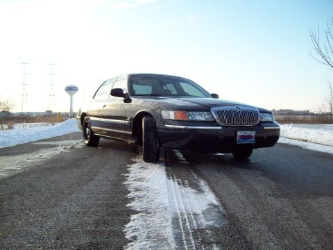 1999 Mercury Grand Marquis - A black Mercury Grand Marquis is seen from the front-right on a road with patches of snow and ice.