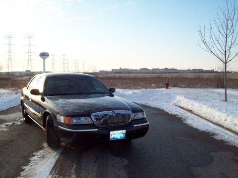1999 Mercury Grand Marquis - Black Mercury Grand Marquis parked on a snowy road with power lines and a water tower in the distance.
