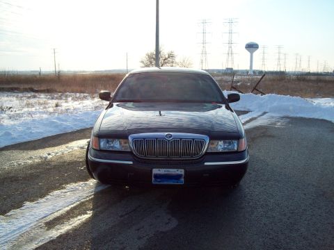 1999 Mercury Grand Marquis - A dark-colored Mercury Grand Marquis is parked on a road with snowbanks, facing the camera on a sunny day.
