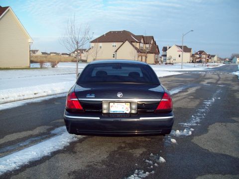 1999 Mercury Grand Marquis - Straight-on rear view of a dark blue Mercury Grand Marquis GS sitting on a wet suburban street with snow on the lawns. A blue '4.6' decal s…