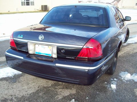 1999 Mercury Grand Marquis - Rear three-quarter view of a dark navy blue Mercury Grand Marquis LS sedan on a snowy driveway, showing the red wraparound taillights, chro…