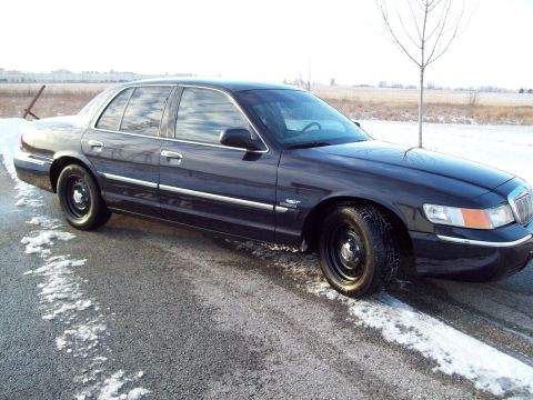 1999 Mercury Grand Marquis - A dark sedan with steel wheels is parked on a road with patches of snow and ice.