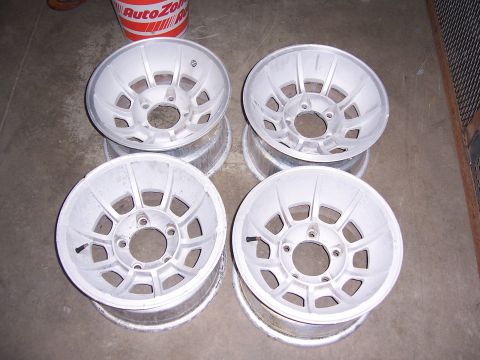 1979 Ford Bronco - Four aluminum alloy wheels are shown stacked on a concrete floor.