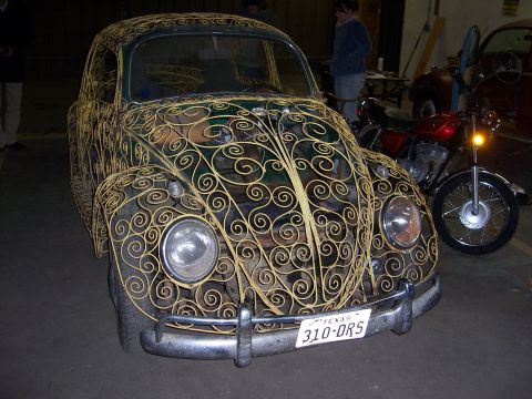 1979 Ford Bronco - A vintage Volkswagen Beetle is adorned with intricate yellow scrollwork, parked indoors with a motorcycle nearby.
