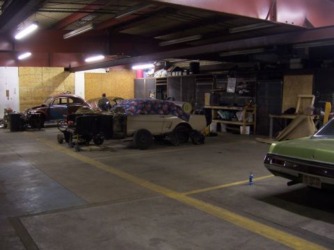 1979 Ford Bronco - A garage scene displays several vintage vehicles in various states of repair, with one car disassembled in the center.