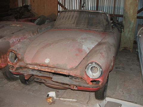 1965 Ford Mustang - This dusty red convertible appears to be in a state of disrepair, parked indoors with another vehicle.