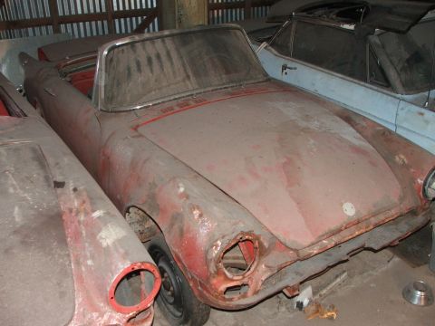 1965 Ford Mustang - A neglected red convertible sports car sits in storage, its condition suggesting it is not a 1965 Ford Mustang.
