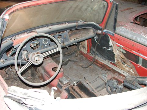 1965 Ford Mustang - The interior of this old red convertible shows significant wear and tear, with a cracked windshield and missing interior components.