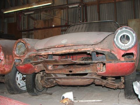 1965 Ford Mustang - This heavily rusted vehicle's front end is visible, showing missing headlights and grille, suggesting it is in a state of disrepair.