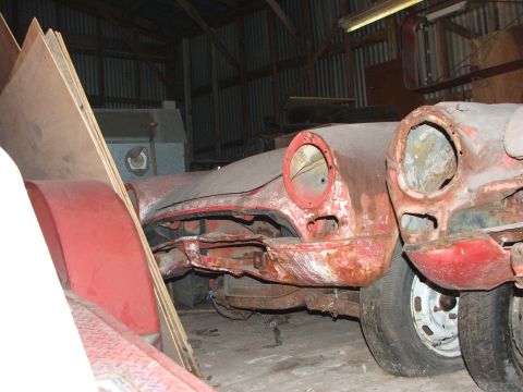 1965 Ford Mustang - Two heavily rusted car front ends sit side-by-side in a dimly lit barn, awaiting restoration.