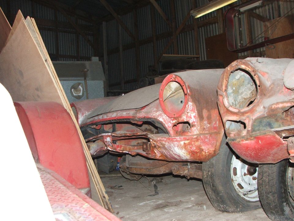 two rusty car front ends, one with a round headlight opening, parked close together in a barn