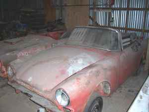 1965 Ford Mustang - A weathered red convertible sports car sits in a dusty garage, awaiting restoration.