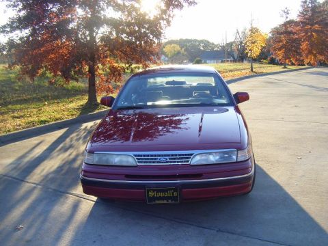 1994 Ford Crown Victoria - A red sedan is parked on a street with trees in the background during autumn.