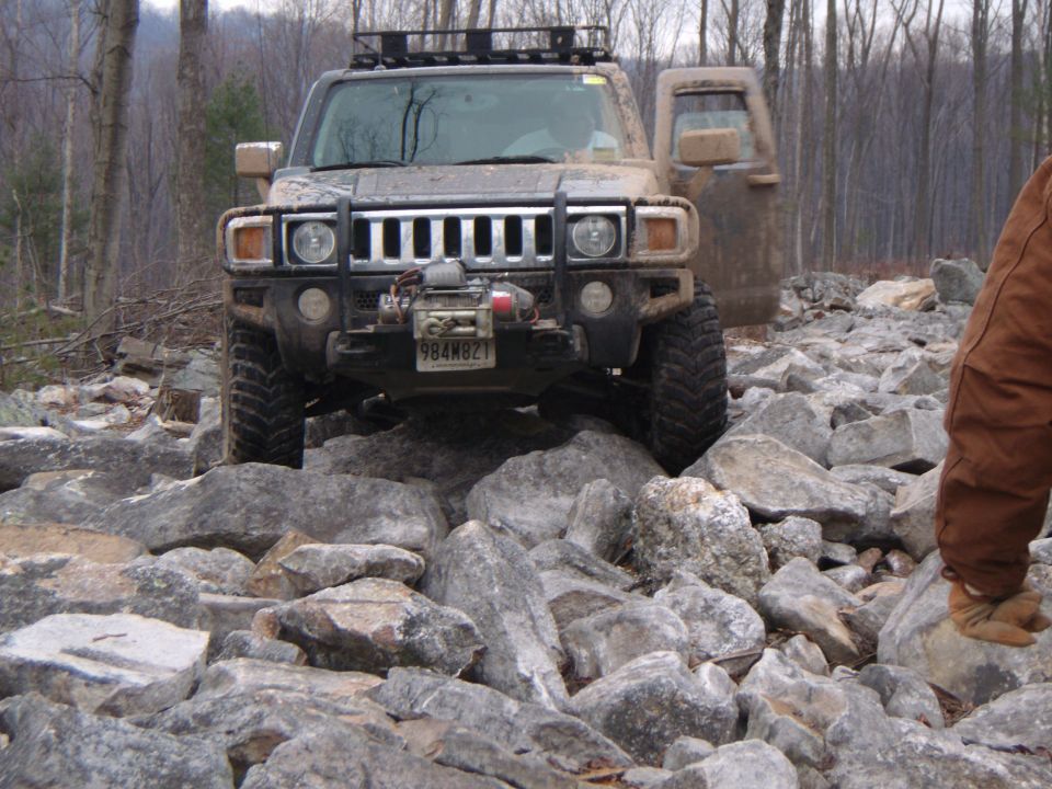 Hummer H3 with winch and roof rack navigating a rocky trail, driver's door open
