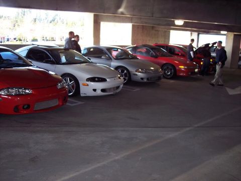 1991 Mitsubishi Eclipse - A line of Mitsubishi Eclipses are parked in a covered lot, with several people standing around.