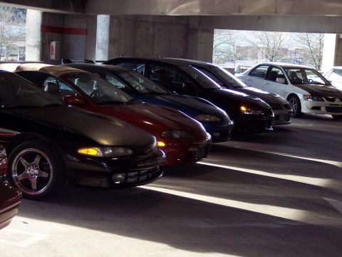 1991 Mitsubishi Eclipse - A line of Mitsubishi Eclipses and a white sedan are parked in a concrete garage with light casting shadows.