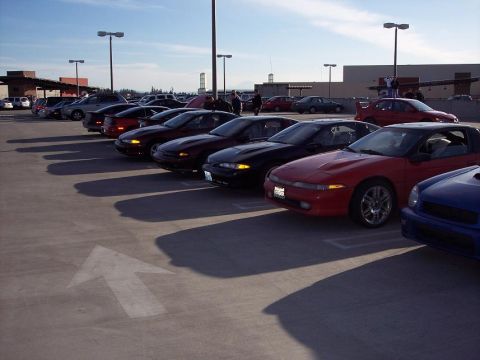 1991 Mitsubishi Eclipse - A row of cars are parked in a lot under a partly cloudy sky.